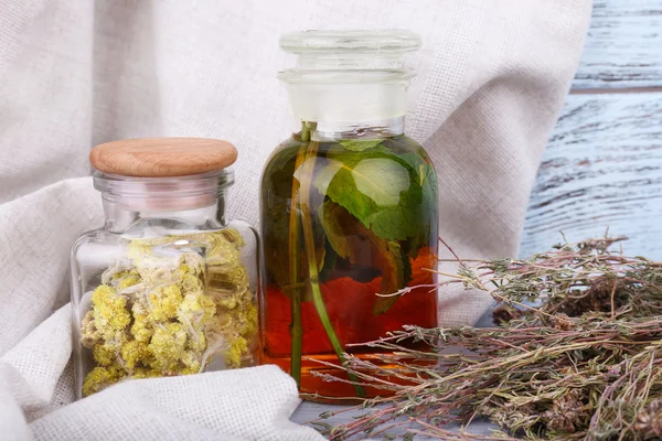 Bottles of herbal tincture and dried herbs on a napkin on wooden background in front of curtain