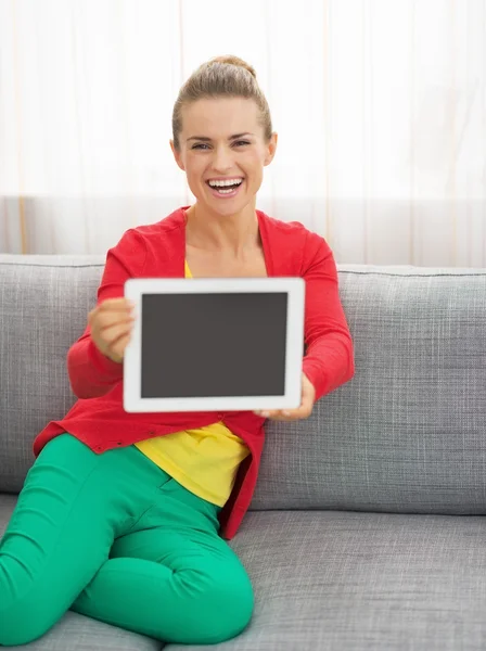 Happy young woman sitting on couch and showing tablet pc