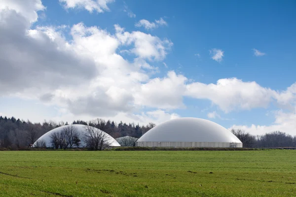 Biogas plant behind a wide field against blue sky