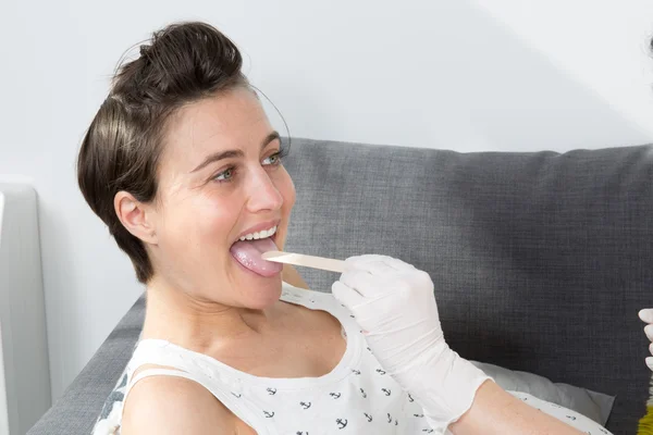 Nurse putting tongue depressor into Caucasian pregnant woman\'s mouth.