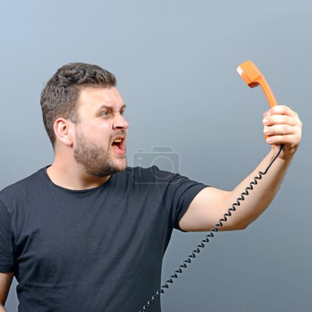 portrait of funny chubby man shouting on phoner against gray bac